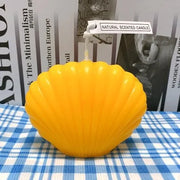 Yellow shell-shaped candle on a blue checkered tablecloth with a magazine background.