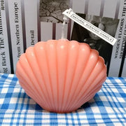 Pink shell-shaped candle on a blue and white checkered tablecloth with a blurred background.
