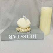 Decorative shell on a braided base with a candle next to it on a gray surface.