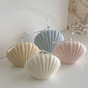 Four shell-shaped candles in pastel colors on a white surface.