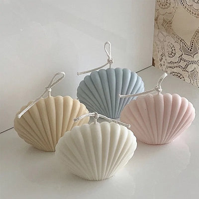 Four shell-shaped candles in pastel colors on a white surface.